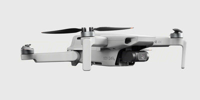 Grå DJI Mini 4K drone fra Fly More Combo pakken vist skråt forfra med foldede arme på hvid baggrund.