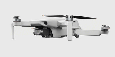 Grå DJI Mini 4K drone i luften over en kyststrækning med blåt vand og grønne klipper.