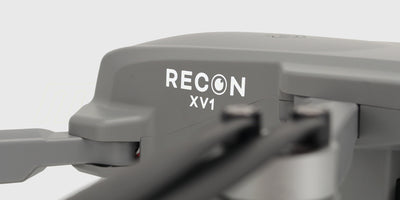 Grå Drone Recon XV1 med foldbare arme og kamera set skråt forfra på hvid baggrund.