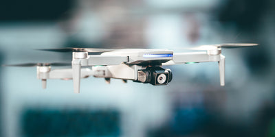 Grå Drone Recon XV1 med brushless motorer flyver i lav højde over en græsplæne.