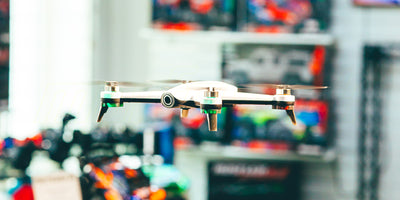 Sort Drone ST16B med fire rotorer flyver stabilt i luften mod en lys baggrund.