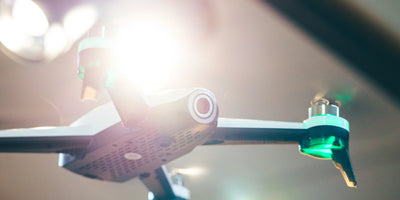 Sort Drone ST16B svæver stabilt i luften over en grøn græsmark i dagslys.