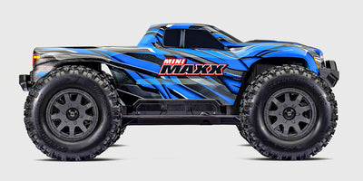 Blå Traxxas Mini Maxx monstertruck i aktion på grusvej med opsprøjtende støv bag de store dæk.