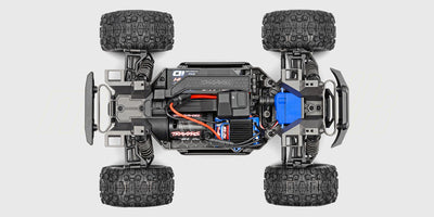 Blå og orange Traxxas Mini Maxx fjernstyret monster truck i et vildt hop over grus og sten.