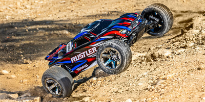 Traxxas Rustler Brushless fjernstyret bil i blå og orange set fra siden med grove offroad-dæk.