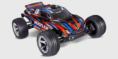 Blå Traxxas Rustler Brushless fjernstyret bil i aktion på en offroad bane.