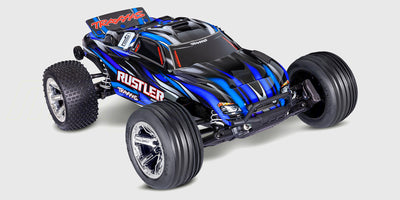 Traxxas Rustler Brushless fjernstyret bil i blå og orange farver, der kører hurtigt gennem støvet i terrænet.