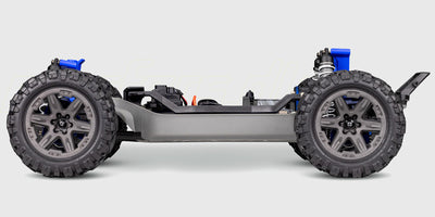 Blå Traxxas Rustler 4x4 BL-2S fjernstyret stadium truck i høj fart på en grusvej med støvskyer bag sig.