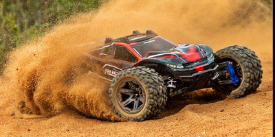 Traxxas Rustler 4x4 BL-2S fjernstyret bil i fuld fart på en grusvej med støvskyer bag de store dæk.