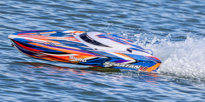 Traxxas Spartan SR speedbåd med blåt og orange grafik ses fra siden i høj fart på vandet.