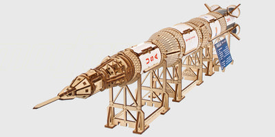 Ugears mekanisk byggesæt af NASA Saturn V raket i lyst træ med detaljerede moduler og udstillingsstander.